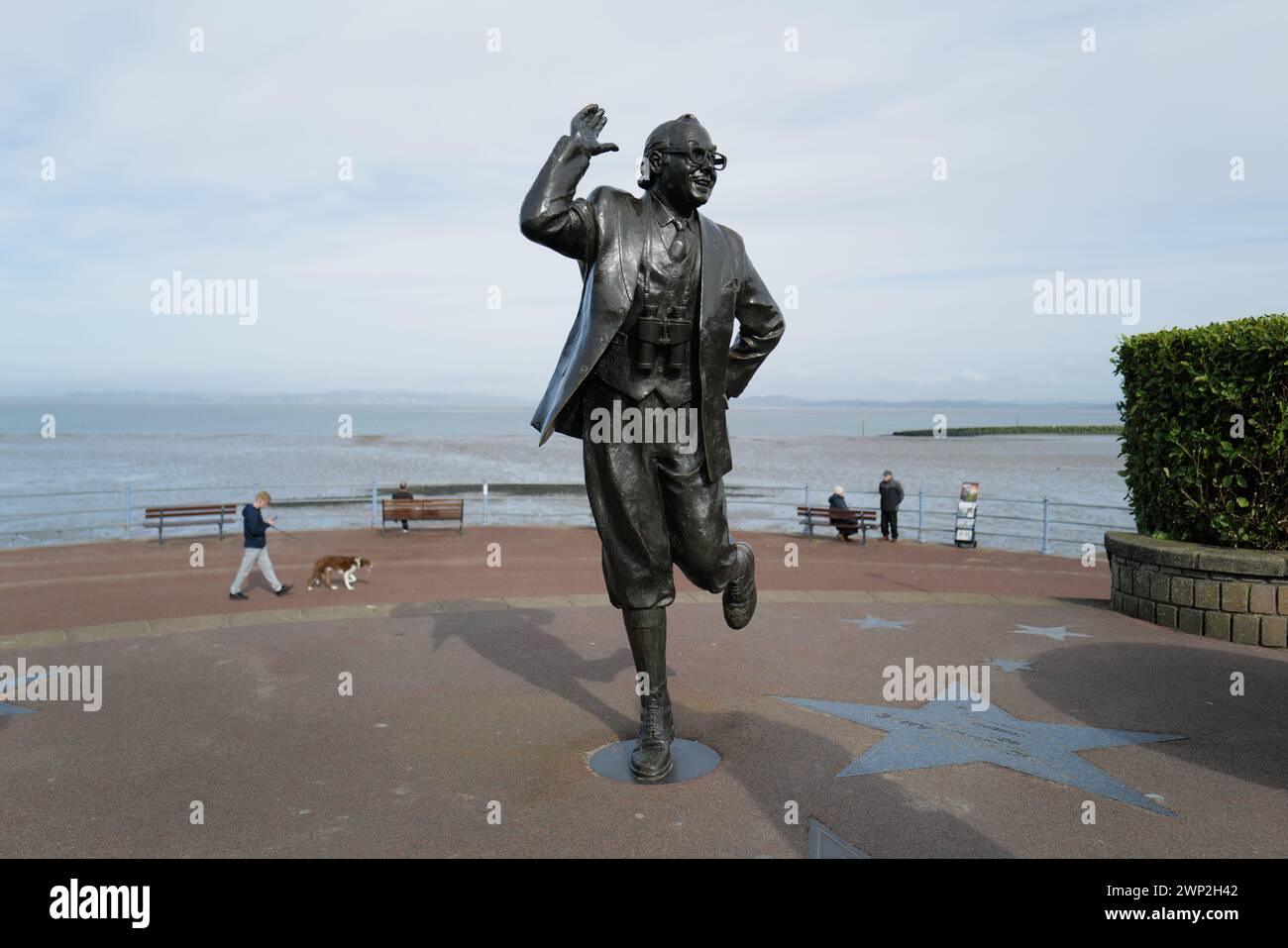 Statua di Eric Morecambe che si affaccia sul mare a Morecambe, Lancashire. Svelata dalla regina nel 1999, la statua leggermente più grande di quella a grandezza naturale raffigura Eric Morecambe in una delle sue pose caratteristiche con un paio di binocoli intorno al collo (era un appassionato ornitologo). La statua si trova sullo sfondo mozzafiato della baia di Morecambe e delle colline del Lake District Foto Stock