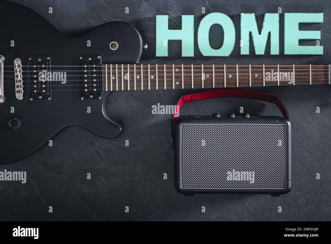 Chitarra elettrica e amplificatore su sfondo scuro con la parola decorativa Home. Foto Stock