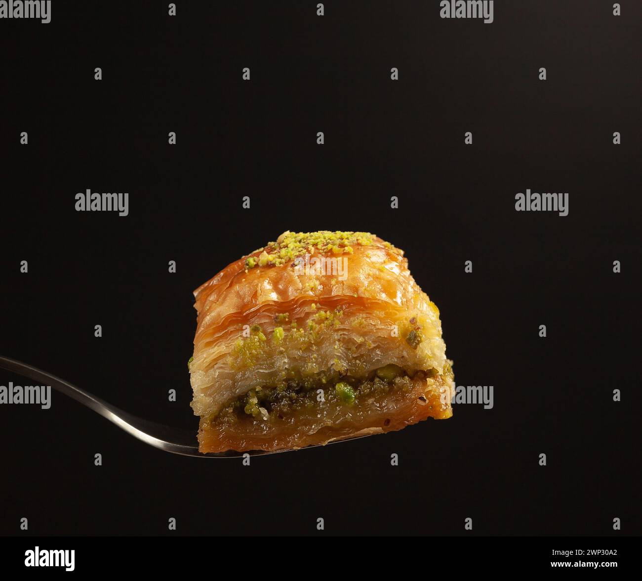 un delizioso baklava al miele con pistacchi su una forchetta su sfondo nero, vista laterale Foto Stock