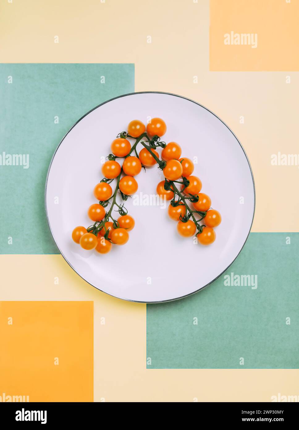 pomodori ciliegini arancioni sui rami su un piatto bianco, sfondo di rettangoli di carta colorata verde e giallo, piano Foto Stock