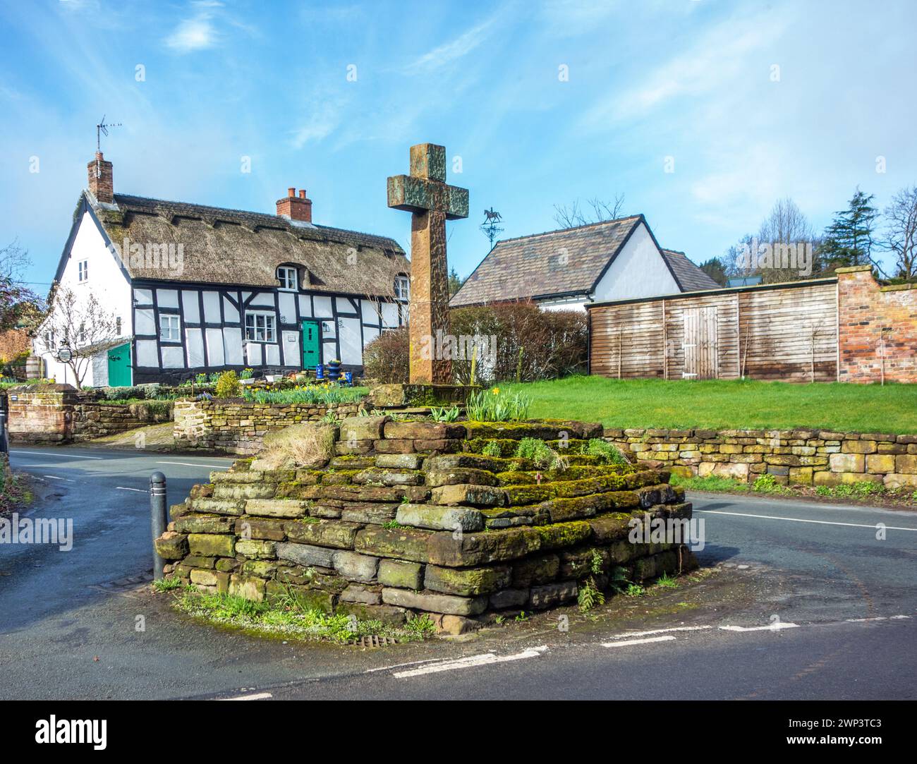 Croce in pietra nel pittoresco e idilliaco villaggio Cheshire di Eaton di Tarporley con un cottage bianco e nero con tetto in paglia in legno Foto Stock