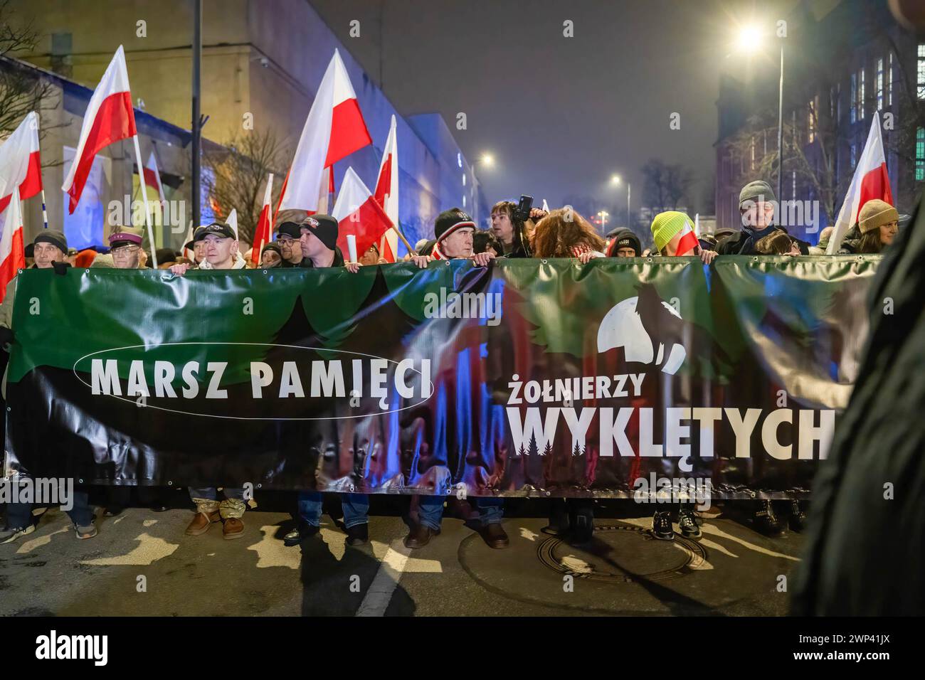 I manifestanti tengono uno striscione con l'iscrizione: "Marcia della memoria dei soldati maledetti", mentre altri sullo sfondo tengono bandiere polacche. Diverse centinaia di persone hanno preso parte alla marcia della memoria dei soldati maledetti a Varsavia. Foto Stock