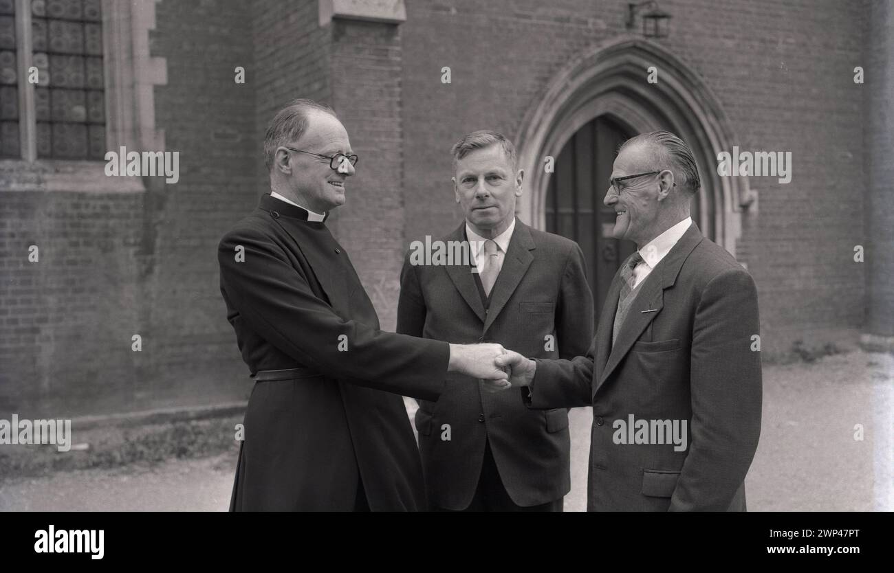 Anni '1950, storico, un ecclesiastico inglese, reverendo A. S Wye, fuori dal vicarage salutando i suoi nuovi guardiani, Oxford, Inghilterra, Regno Unito. Il XIII secolo vide apparire dei guardiani, membri di una congregazione eletti da e tra i parrocchiani, per rappresentare quelli di una fede religiosa, i laici e assumersi la responsabilità del tessuto della chiesa, dell'amministrazione e di altri doveri. Foto Stock