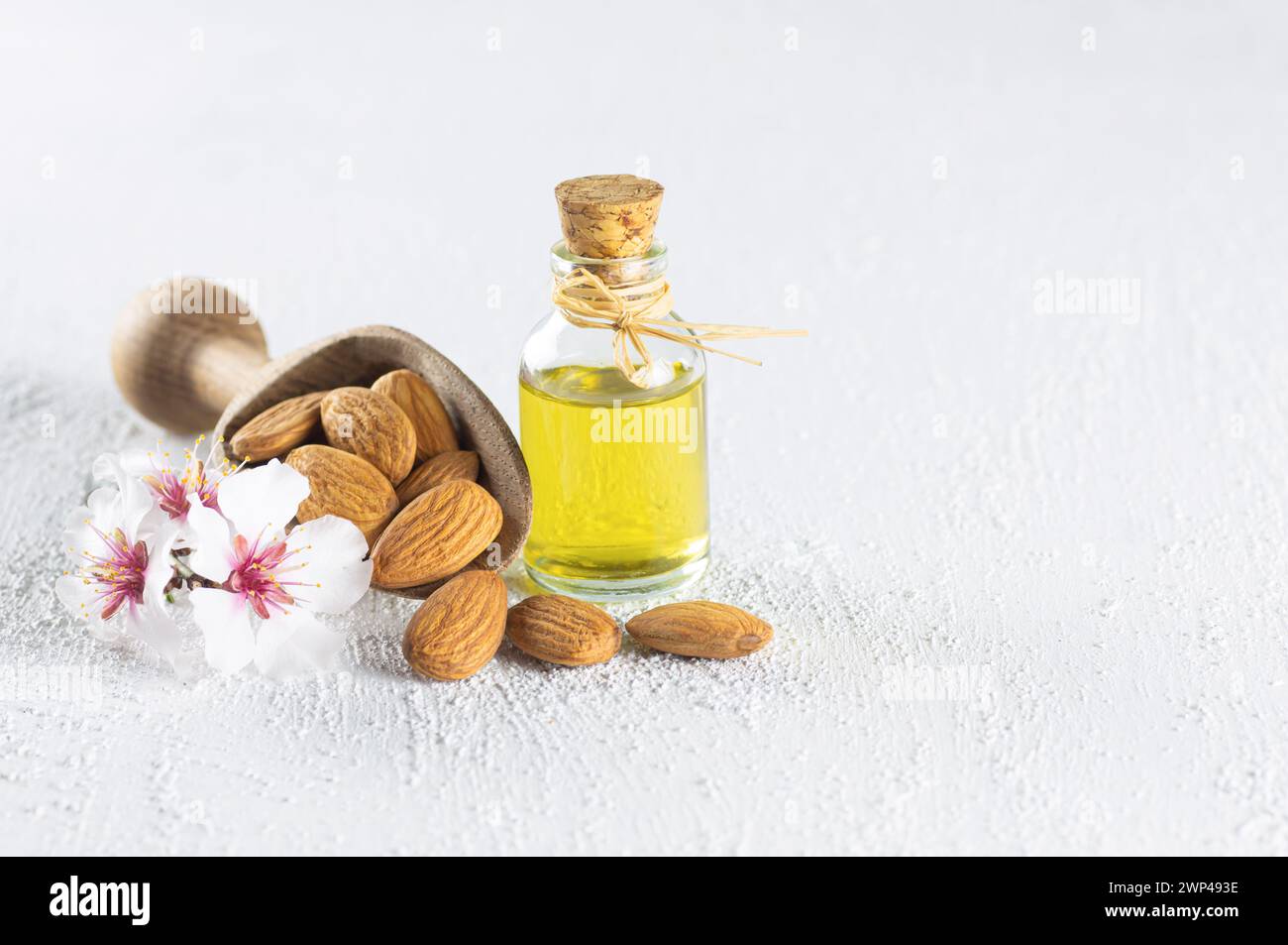 Bottiglia in vetro di olio di mandorle e noci di mandorle, mandorle con fiori di mandorle sul tavolo. Concetto di sfondo Almond con spazio di copia Foto Stock