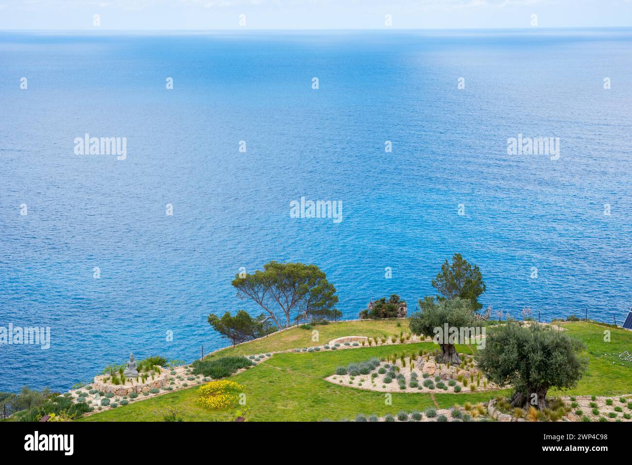 Tranquilla vista mare con giardino terrazzato, aree verdi erbose, letti rocciosi e alberi in primavera, giardino roccioso con erba, lavanda (Lavandula), rosmarino Foto Stock