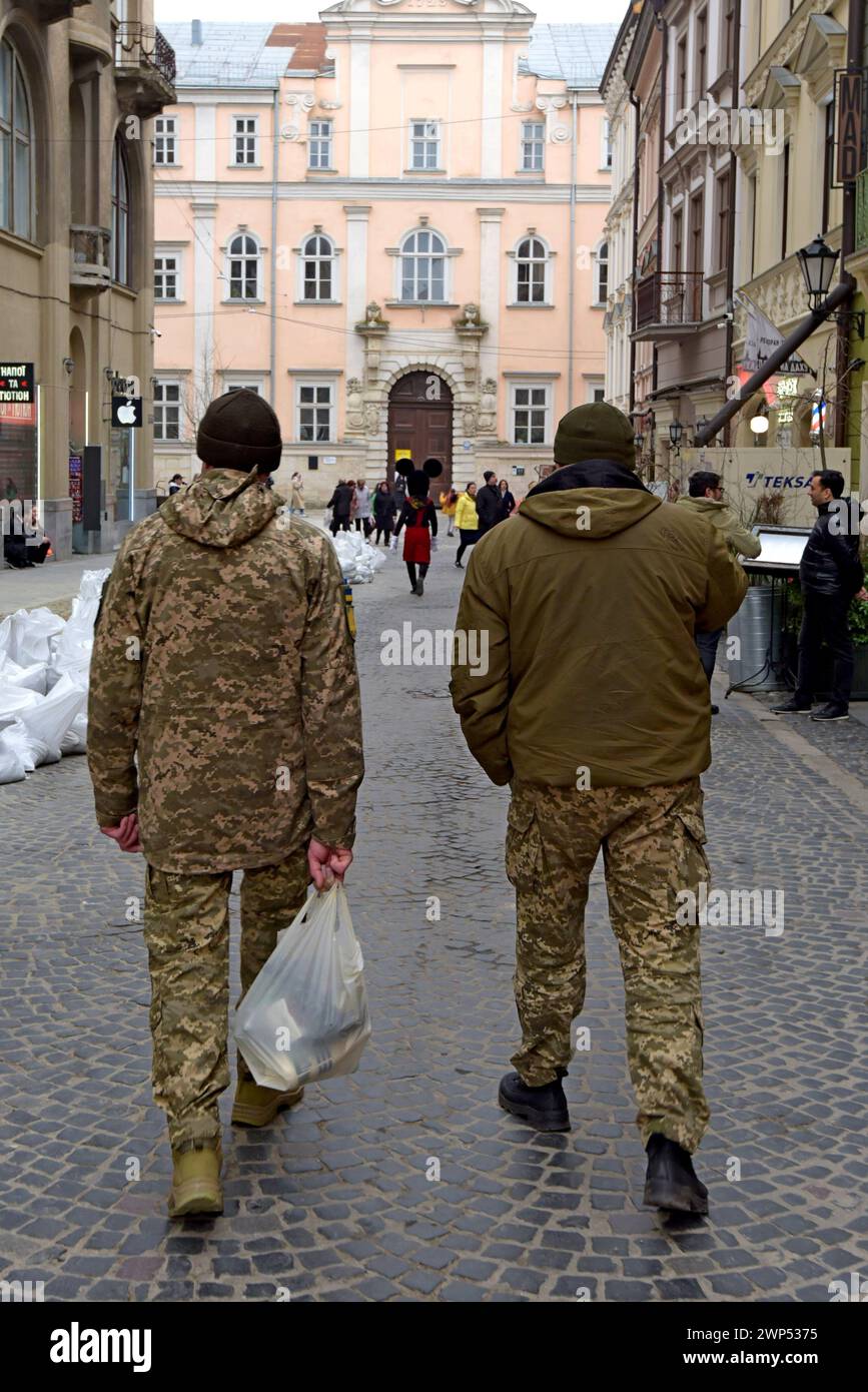 Soldati in Leave che camminano dietro una persona in costume di topolino, centro città di Leopoli, Ucraina, marzo 2024 Foto Stock