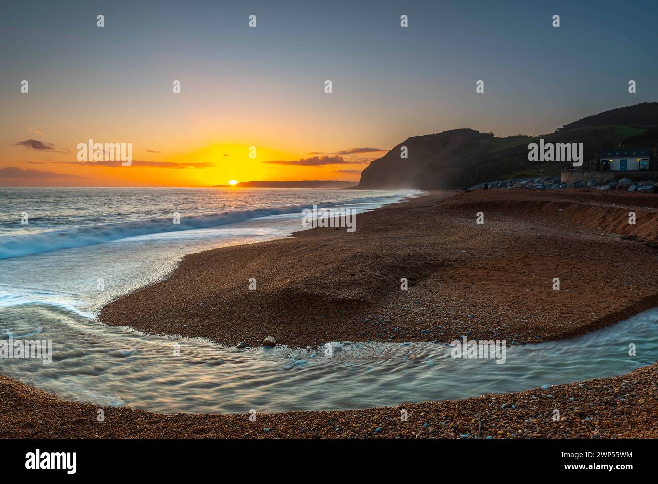 Seatown, Dorset, Regno Unito. 5 marzo 2024. Meteo nel Regno Unito. Il fiume Winniford scorre attraverso la spiaggia al tramonto a Seatown sulla Dorset Jurassic Coast guardando verso le scogliere del Golden Cap mentre il cielo limpido dopo una mattina di pioggia. Crediti fotografici: Graham Hunt/Alamy Live News Foto Stock