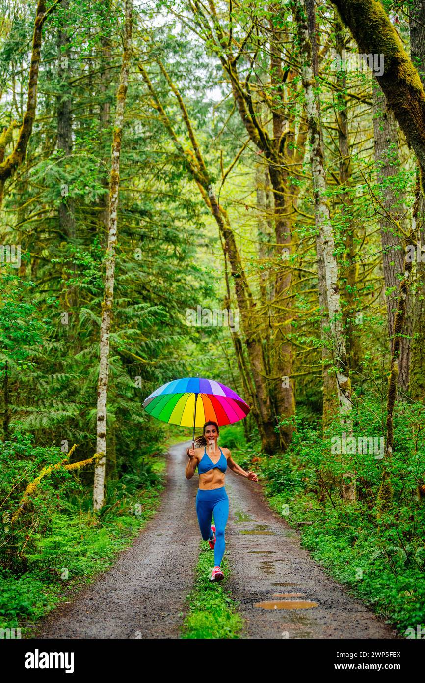 Donna che corre con ombrello e indossa abiti da ginnastica Foto Stock