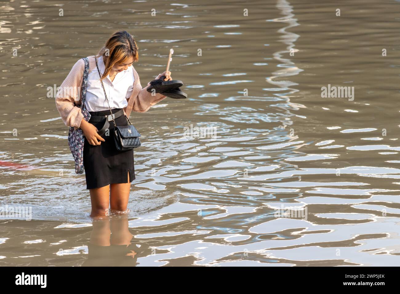 SAMUT PRAKAN, TAILANDIA, 11 febbraio 2024, Una donna sorridente aspetta attraverso una strada allagata Foto Stock