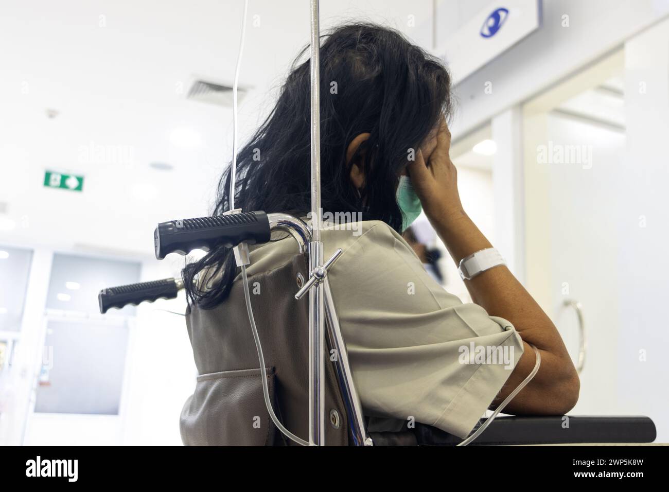 Un paziente con un'infusione è seduto su una sedia a rotelle in attesa di essere esaminato da un medico Foto Stock