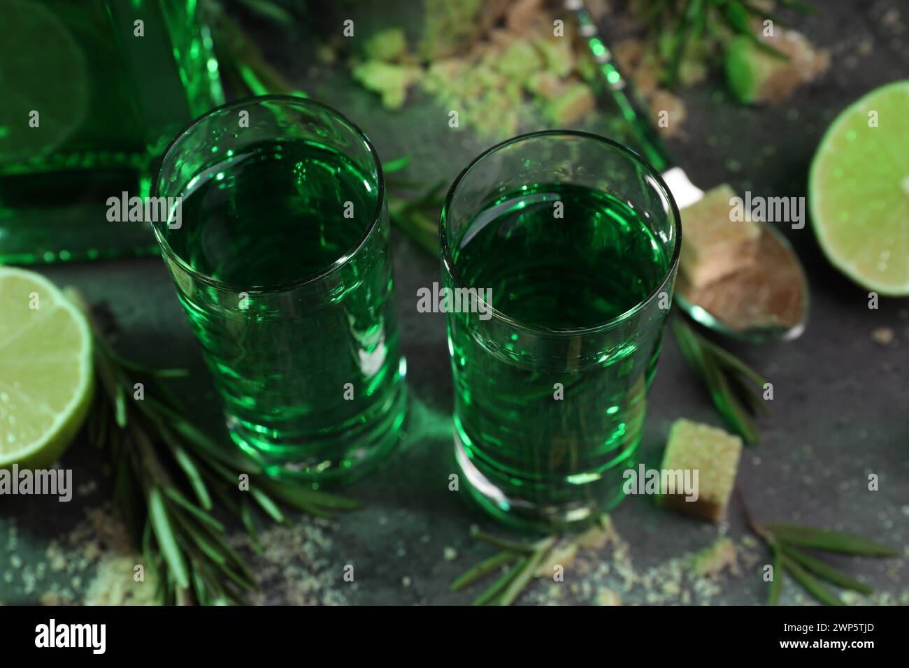 Absinthe in bicchieri da shot, zucchero di canna, lime e rosmarino su tavolo grigio, primo piano. Bevanda alcolica Foto Stock