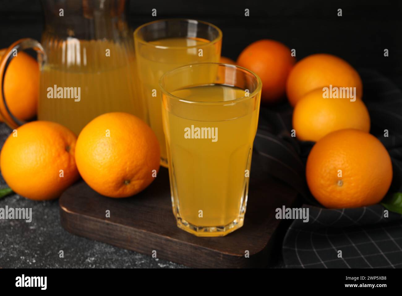 Molte arance mature e succo fresco su un tavolo grigio scuro Foto Stock