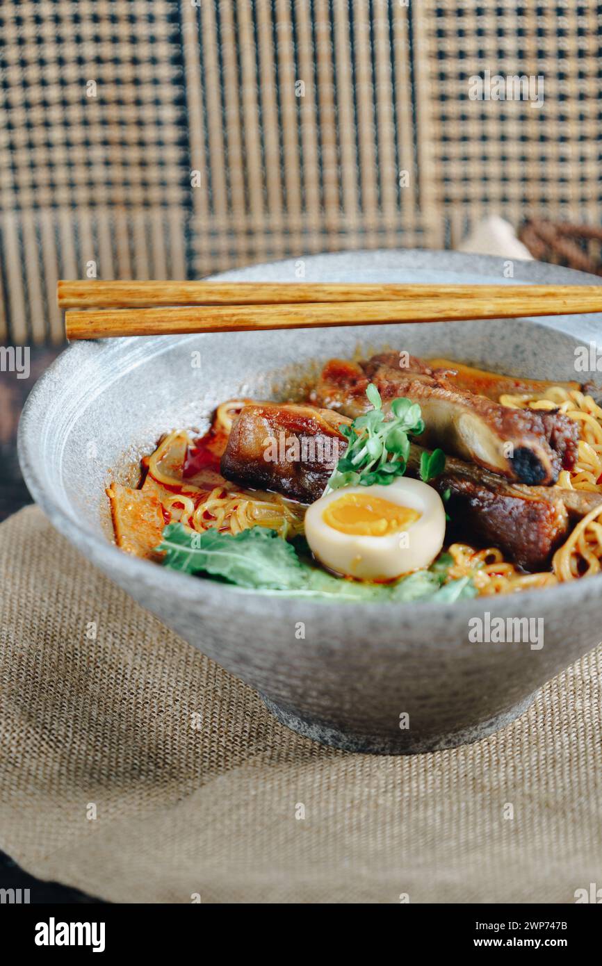 Una ciotola di ramen con carne e uovo. La ciotola si trova su un tavolo con le bacchette accanto Foto Stock