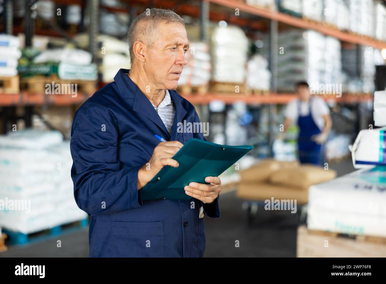 Nel magazzino del negozio, un uomo maturo verifica la disponibilità delle merci e dei documenti di ricevimento per i prodotti Foto Stock