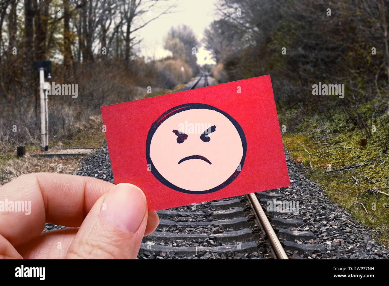FOTOMONTAGE, Hand hält Zettel mit wütendem Emoji vor leeren Bahnschienen, Symbolfoto Bahnstreik Foto Stock