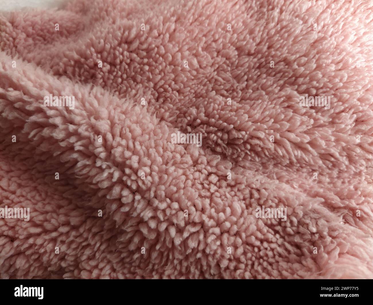 Pelliccia sintetica rosa piegata a onde. Colore rosa sporco pallido del materiale sintetico. Consistenza morbida. Il mucchio di lana si arrotolò in grumi. Frammento del copriletto Foto Stock