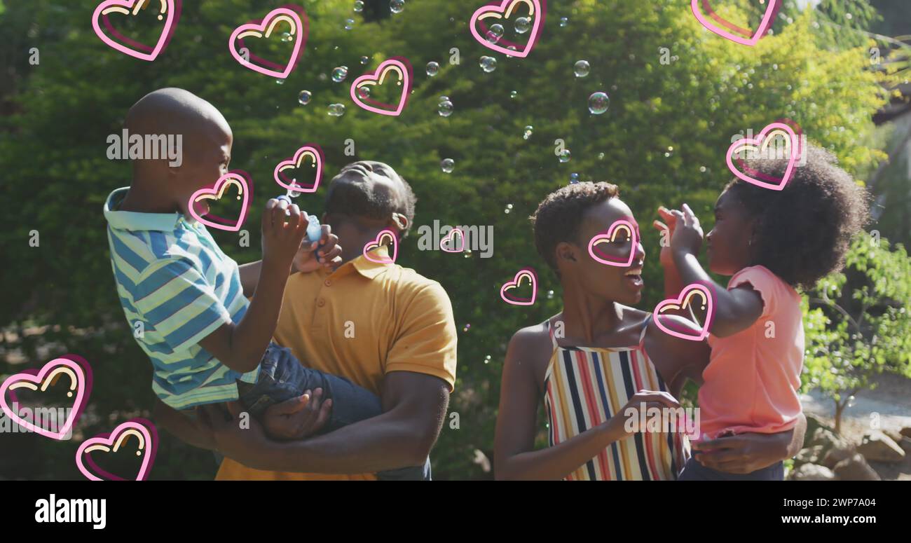 Immagine di cuori su una felice famiglia afroamericana che produce bolle di sapone in giardino Foto Stock
