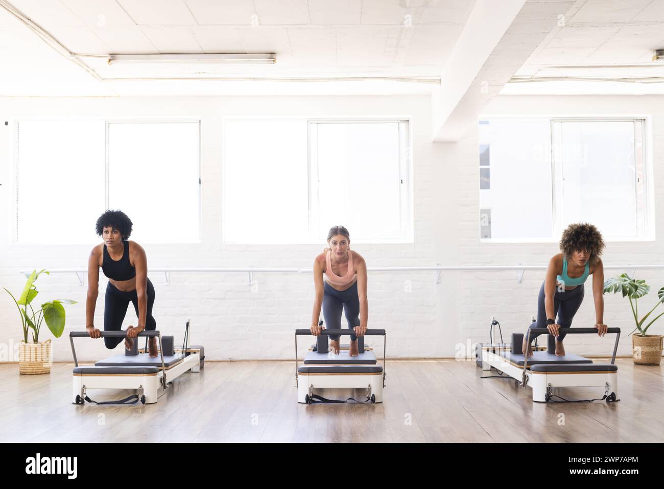 Tre donne si allenano con Pilates in un luminoso studio di riformatori Foto Stock
