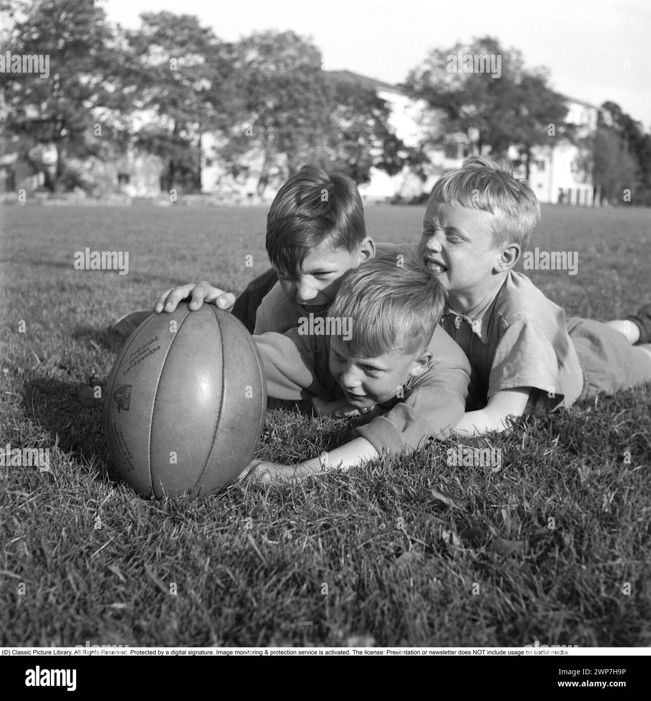 Rugby 1940. Tre giovani giocatori di rugby sdraiati sull'erba del campo da rugby, uno che tiene la palla da rugby. La palla da rugby ha una forma ovale, quattro pannelli e un peso di circa 400 grammi. 1942. Kristoffersson rif. A56-4 Foto Stock