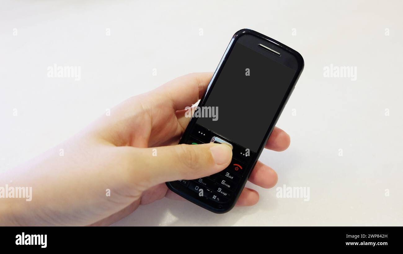 Mano che regge un cellulare nero obsoleto con schermo vuoto. Foto Stock