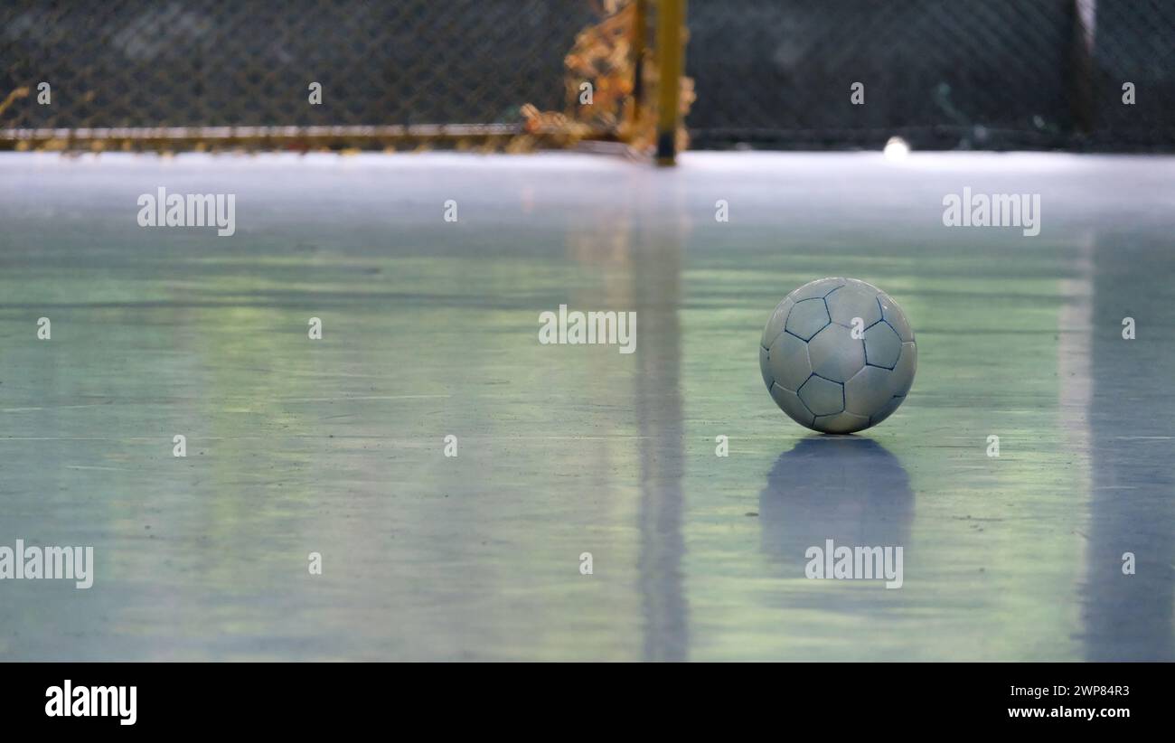 Una palla futsal solitaria, sul terreno di un campo futsal vuoto, con la base della rete goal visibile sullo sfondo. Foto Stock