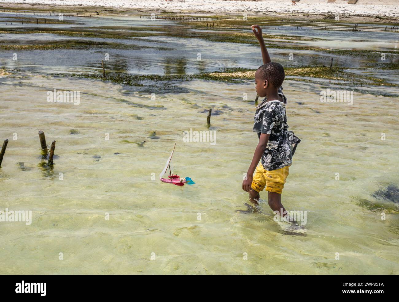 Il bambino gioca con un dhow giocattolo a vela realizzato con sandali di plastica sulla spiaggia di Jambiani, Zanzibar, Tanzania Foto Stock