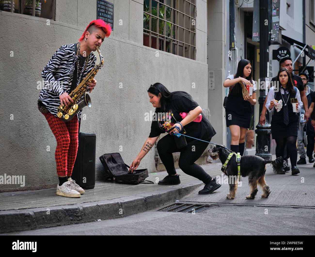 Un gruppo di individui in piedi su un marciapiede con un cane al guinzaglio Foto Stock