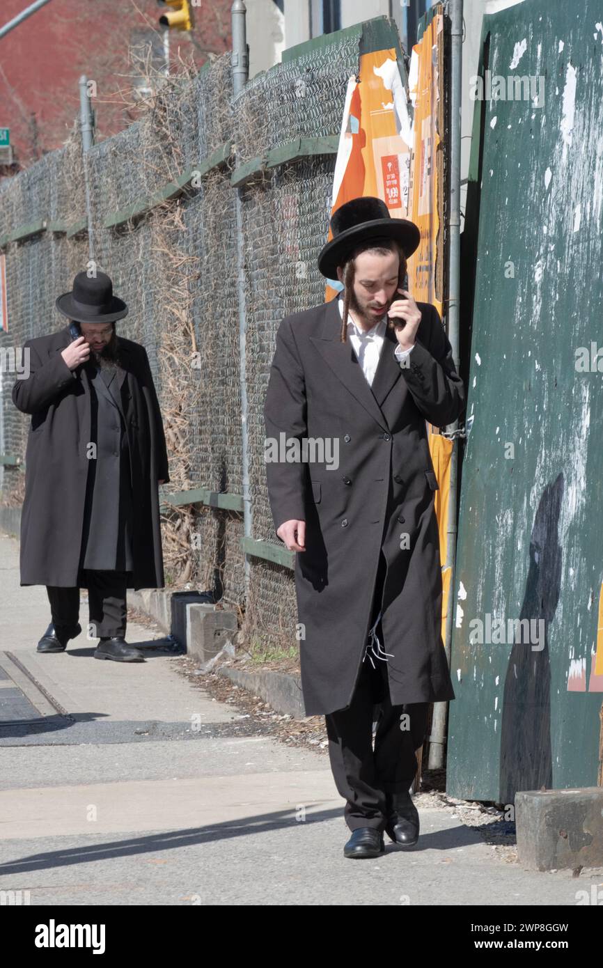 2 ebrei ortodossi camminano separatamente e parlano sui loro telefoni. Su Lee Avenue a Williamsburg, Brooklyn, New York City. Foto Stock