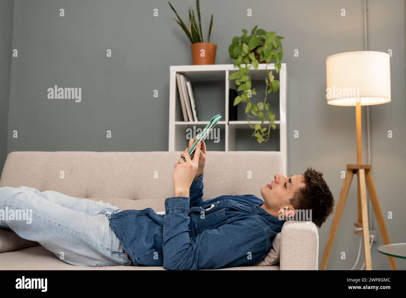 Giovane uomo rilassato e spensierato che guarda video con un tablet a casa. Bell'uomo che riposa con il touchpad mentre è seduto su un divano. Foto Stock