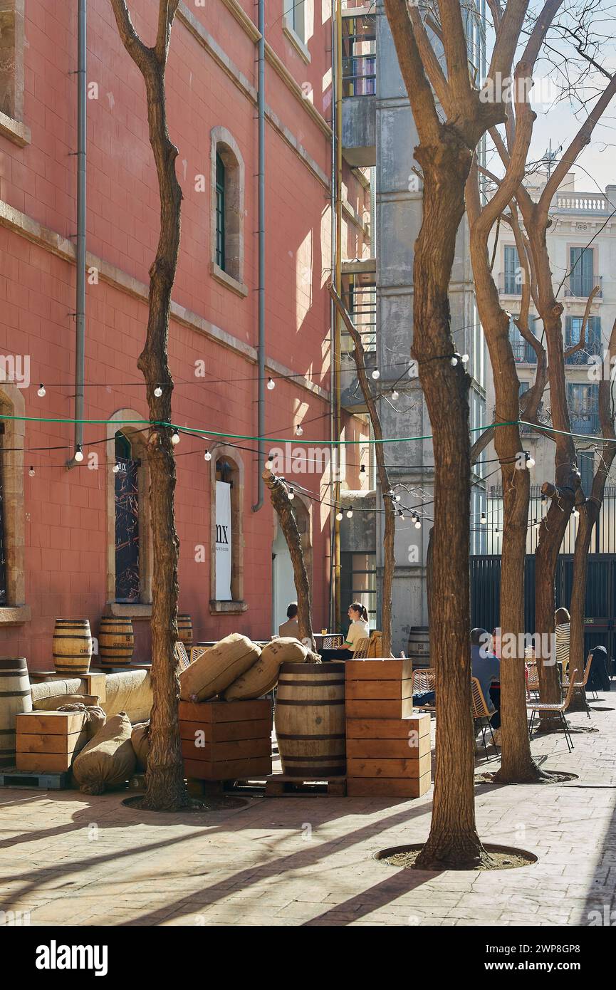 Barcellona, Spagna - 06 marzo 2024: Scena urbana d'epoca con botti di legno, sacchi e alberi che creano un'atmosfera rilassata e nostalgica. Foto Stock