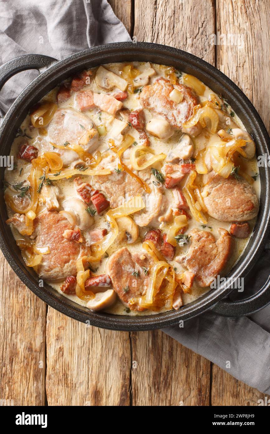 Filetto di maiale danese abbinato a cipolle, pancetta e funghi, il tutto inumidito in una salsa cremosa a primo piano sulla padella sul tavolo. Via superiore verticale Foto Stock