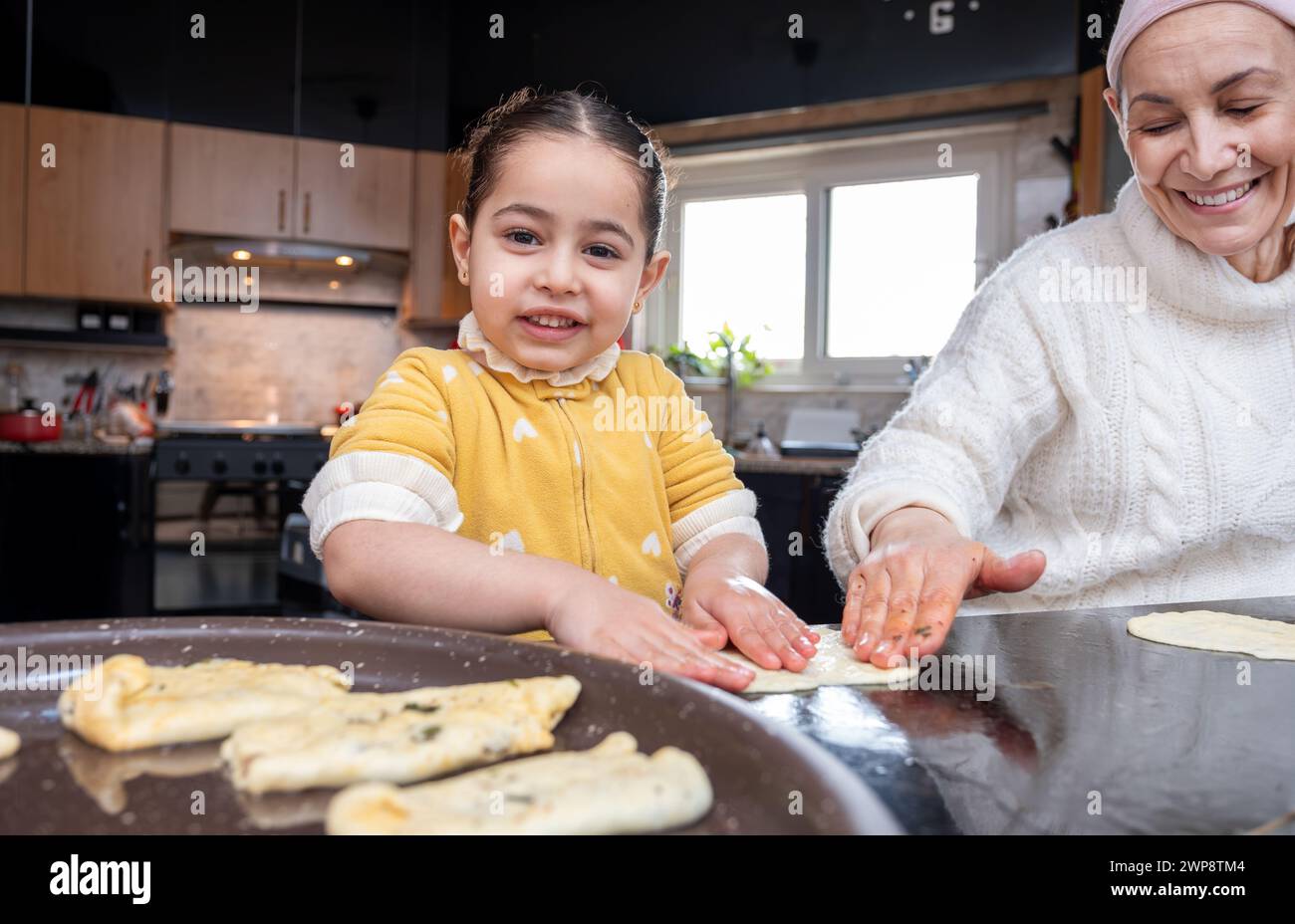 Un'emozionante scena in cui la nonna e il bambino si legano in cucina, tramandando la tradizione culinaria e l'amore attraverso prelibatezze fatte in casa Foto Stock