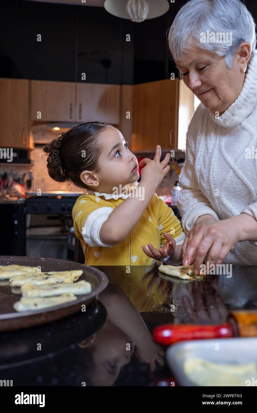 Un'emozionante scena in cui la nonna e il bambino si legano in cucina, tramandando la tradizione culinaria e l'amore attraverso prelibatezze fatte in casa Foto Stock