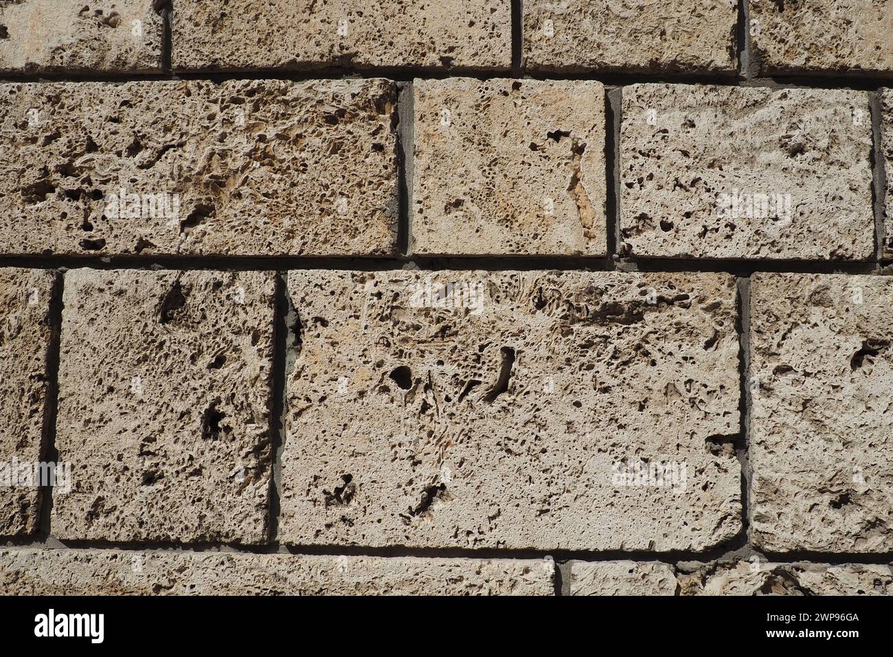 Parete testurizzata rivestita con piastrelle in pietra beige. Primo piano di un muro fatto di antica roccia a conchiglia. Buchi, irregolarità del materiale da costruzione naturale Foto Stock