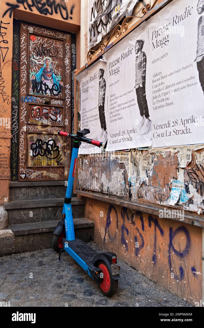 Moderno scooter elettrico a noleggio, parcheggiato vicino a una porta dipinta con graffiti all'angolo di una strada nel quartiere Trastevere. Roma, Italia, Europa Foto Stock