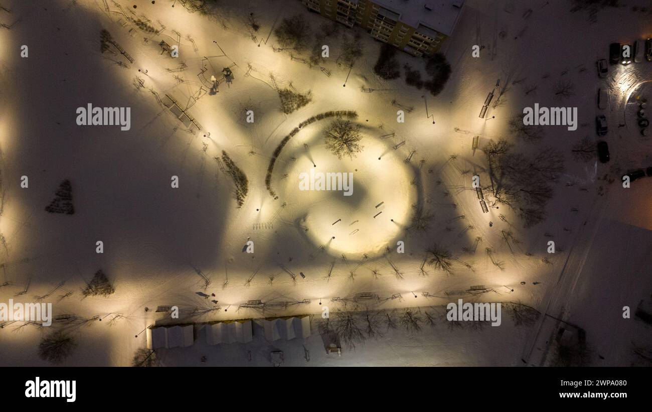 Fotografia con drone di un piccolo parco cittadino e parco giochi coperto di neve durante la notte nuvolosa d'inverno Foto Stock