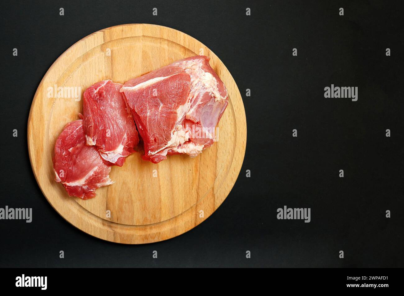 filetto di maiale fresco su un tagliere rotondo in legno su sfondo nero, spazio copia. Foto Stock
