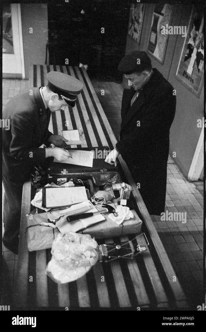Una fotografia del 1959 raffigurante un funzionario doganale che supervisiona l'ispezione delle borse di un viaggiatore presso la stazione estera dell'aeroporto di Varsavia. L'immagine mostra la verifica del passaporto e le procedure standard di controllo dei bagagli. Foto Stock