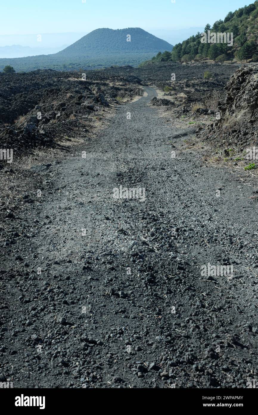 Strada sterrata attraverso il campo lavico nel Parco dell'Etna, all'orizzonte l'antico vulcano del 'Monte Minardo', Sicilia, Italia Foto Stock