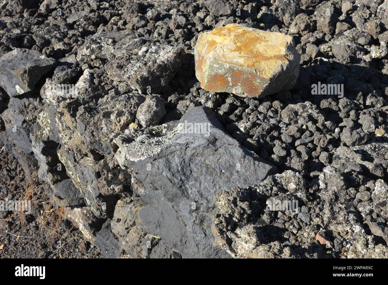 Contrasto di colori di una roccia vulcanica color zolfo e ferro e il colore blu-piombo del basalto sullo sfondo, Parco dell'Etna, Sicilia, Italia Foto Stock