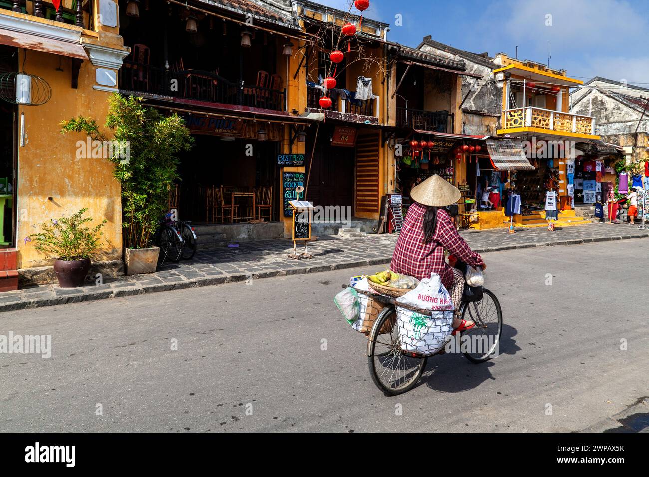 Hoi An, Vietnam; scena di strada dalla città vecchia. Una donna che trasporta la sua merce sulla sua bici Foto Stock