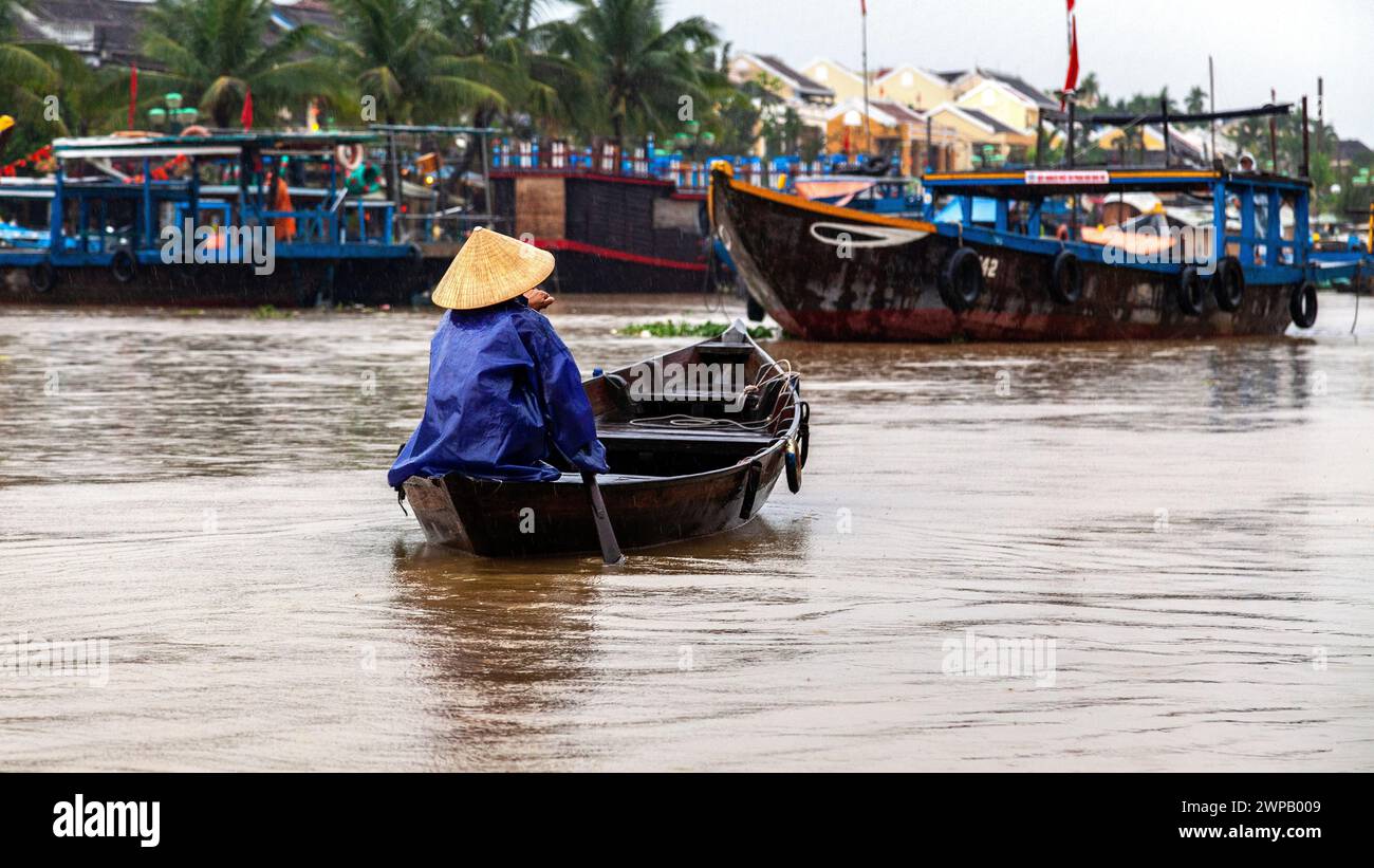 Hoi An, Vietnam; scena dalla città vecchia. Una donna che trasporta in paddler in cerca di passeggeri da trasportare sulla sua barca di legno Foto Stock