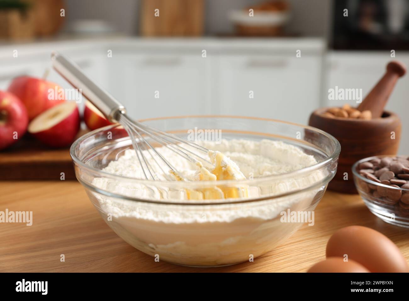 Processo di cottura. Frusta in metallo, recipiente, farina, uova e altri prodotti su un tavolo di legno in cucina, primo piano Foto Stock