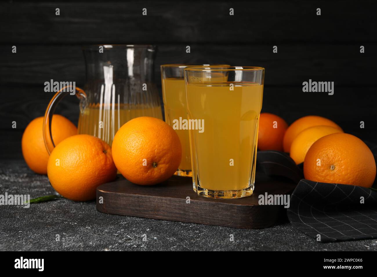 Molte arance mature e succo fresco su un tavolo grigio scuro Foto Stock
