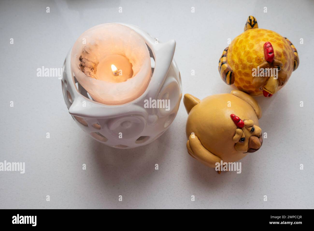 Una candela illuminata accanto a due polli decorativi dall'alto, sfondo bianco. Foto Stock