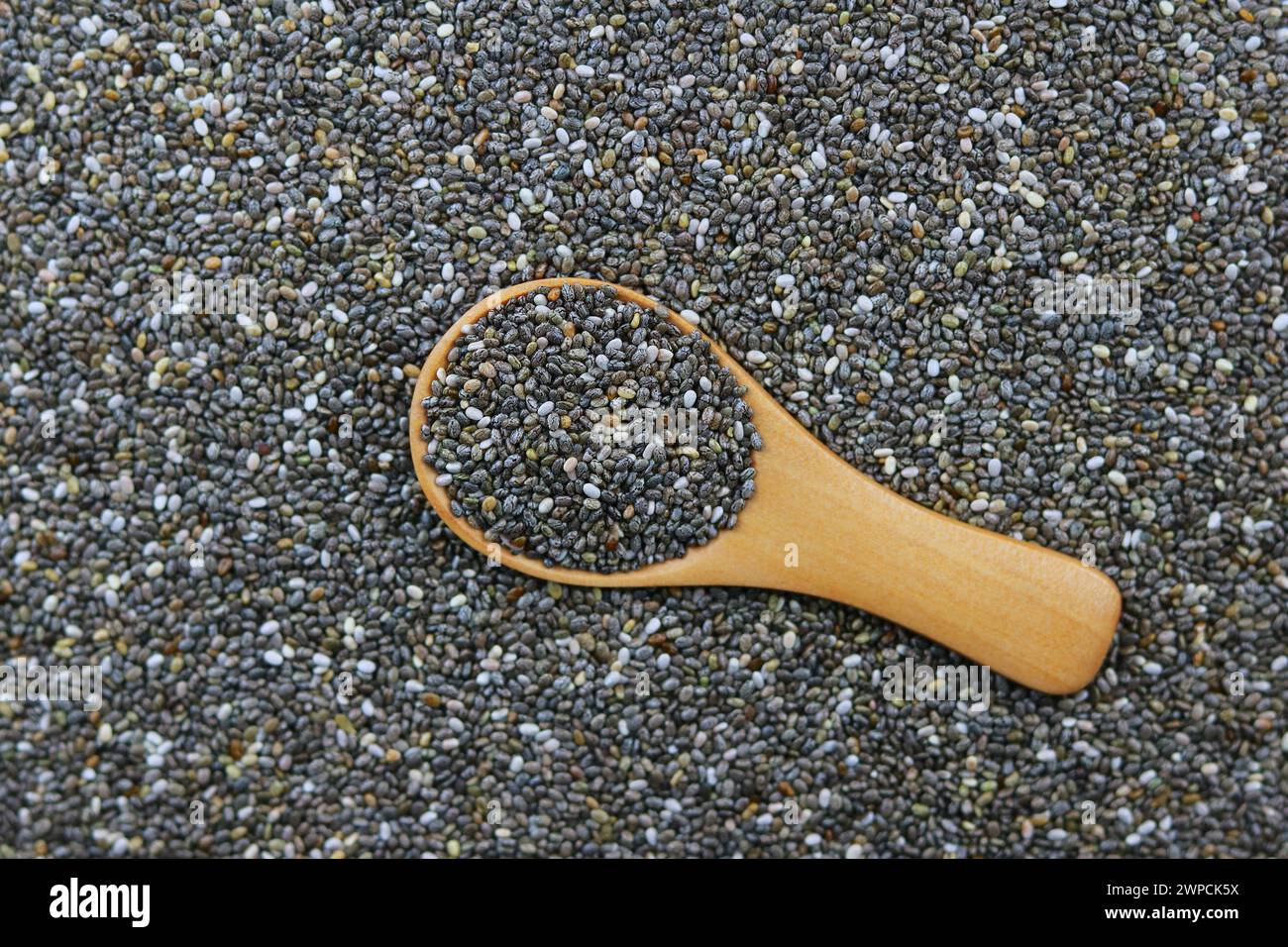 Semi di chia in un cucchiaio di legno su uno sfondo di semi di chia Foto Stock