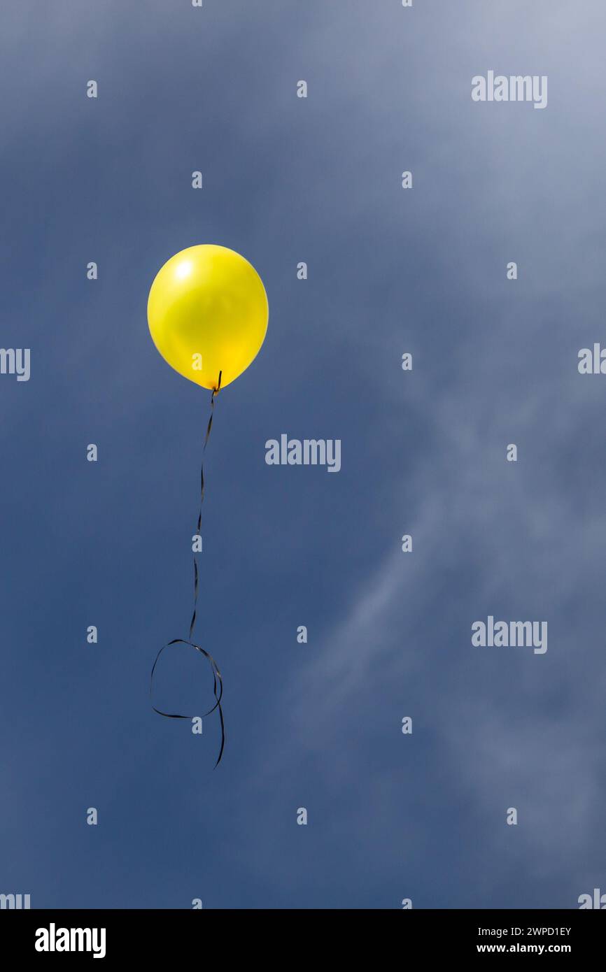 Un palloncino giallo che si sposta in un cielo azzurro Foto Stock