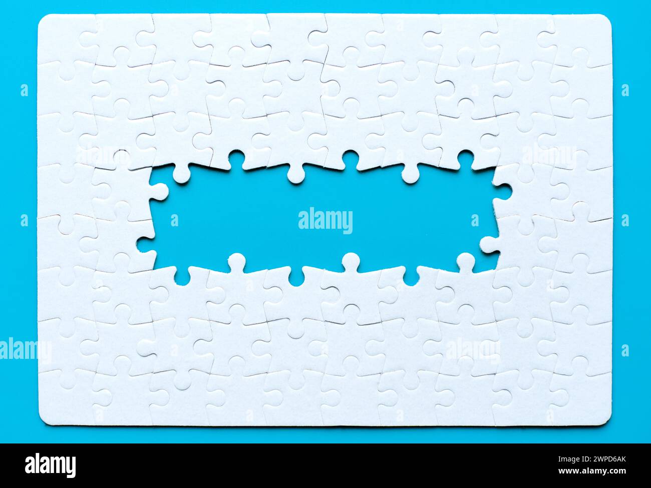 Puzzle vuoto assemblato con diversi pezzi mancanti al centro disposti su uno sfondo blu incontaminato. Concetto di unità e progressione. Foto Stock