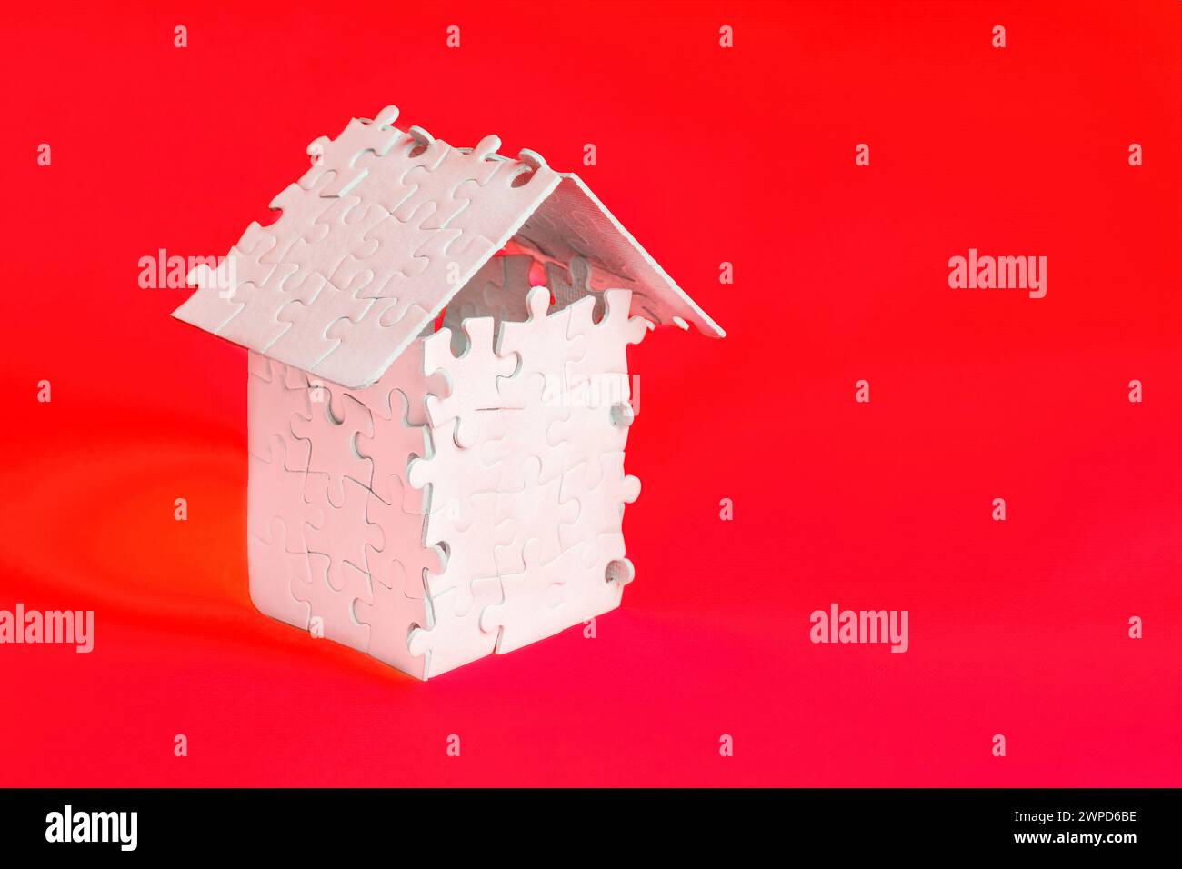 Fogli di puzzle bianchi disposti in un modello di casa in miniatura con un tetto isolato su sfondo rosso. Foto Stock