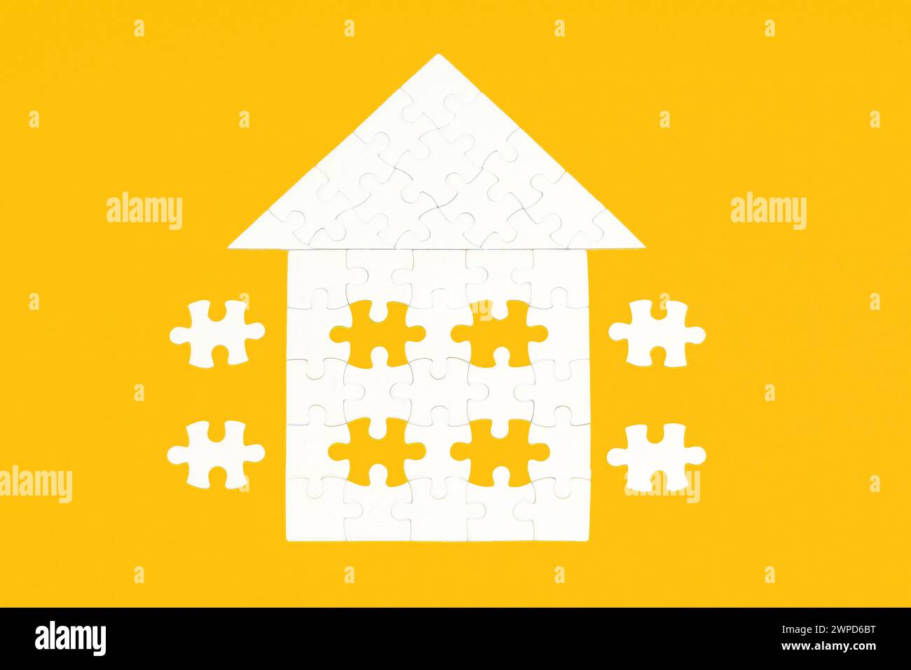 Puzzle bianco a forma di casa sul tetto, posizionato su uno sfondo giallo incontaminato. Alcuni elementi finali sono accantonati. Foto Stock